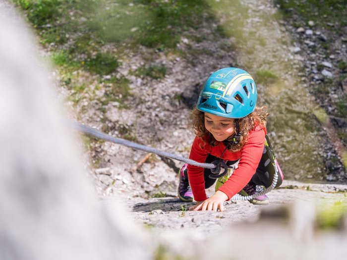 Sexten: a paradise for mountain lovers Child wearing helmet climbing a rock outdoors with safety gear