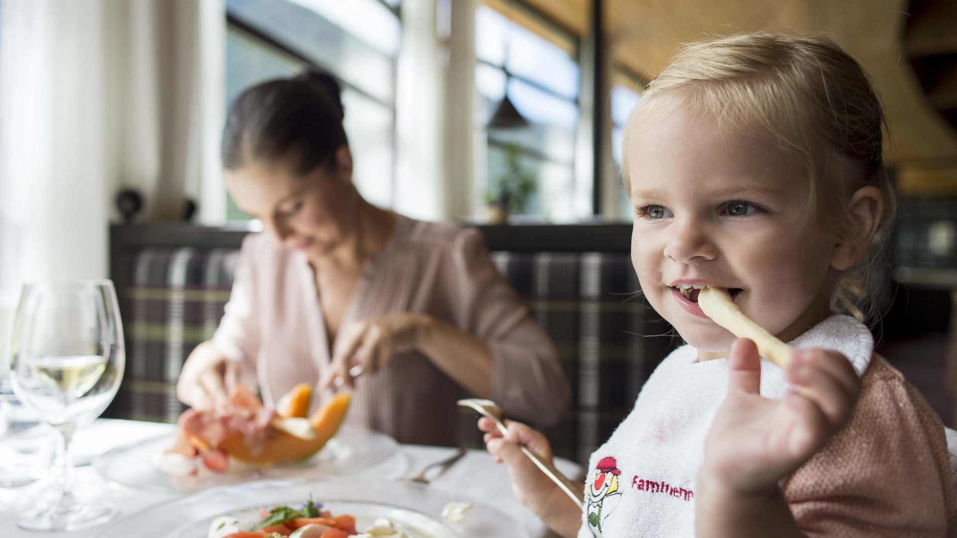 Family Resort Rainer Bambina che mangia patatine in un ristorante con una donna sullo sfondo