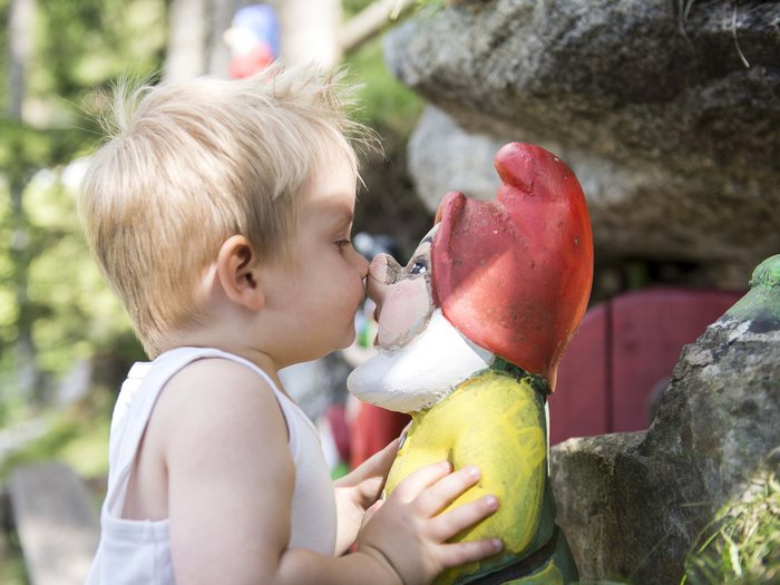 Your hotel with childcare in the Dolomites Little boy kissing a garden gnome statue outdoors