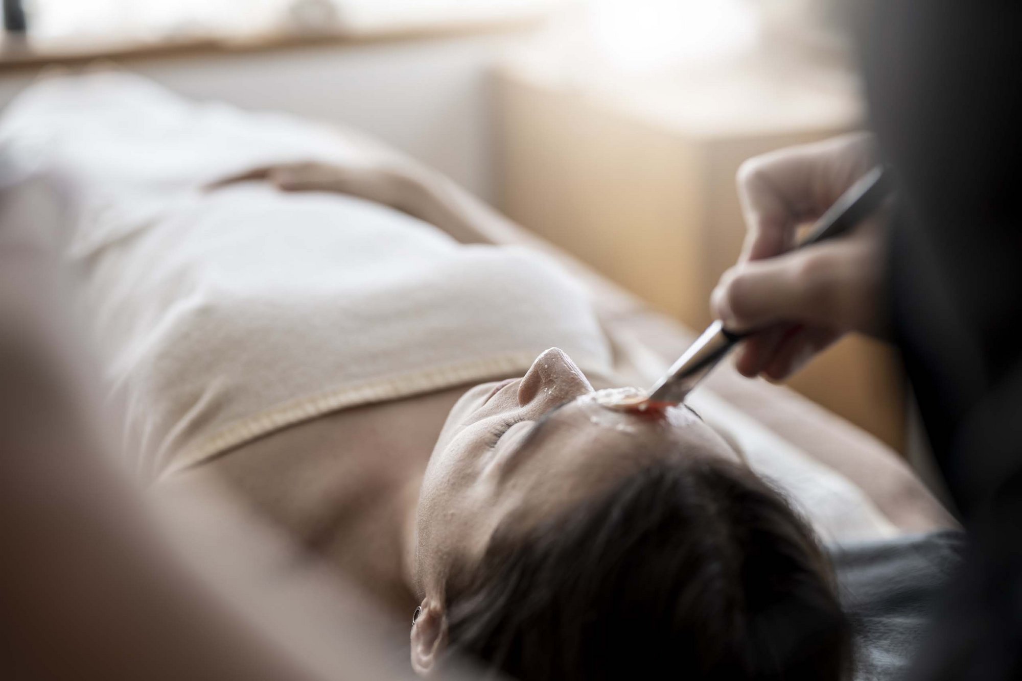 Benessere dalla testa ai piedi Donna sdraiata che riceve trattamento viso con pennello