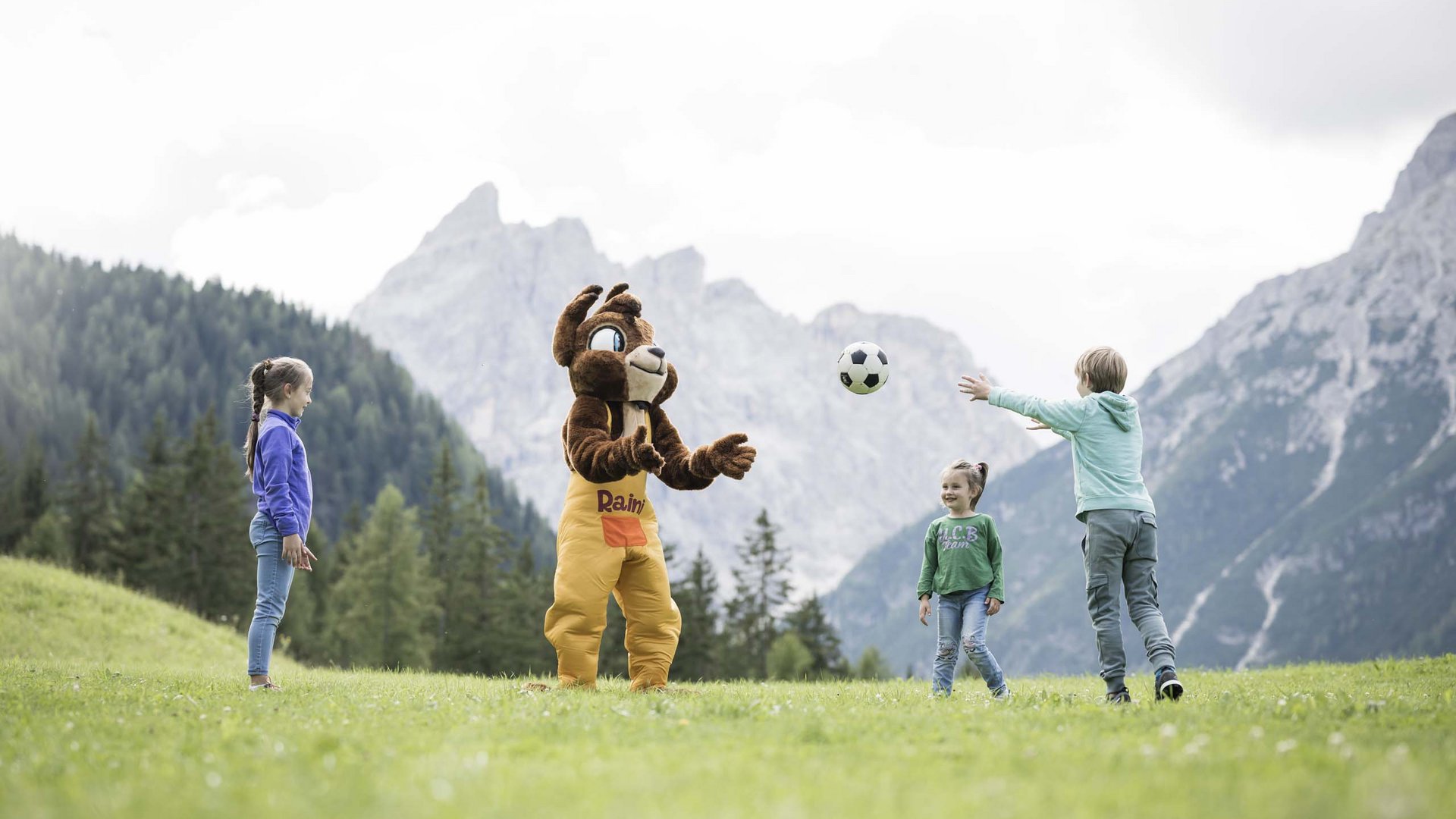 Qualche immagine del Rainer Bambini che giocano a calcio con una mascotte orso su un prato davanti alle montagne