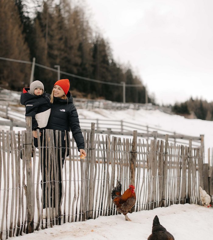 Our family experiences Woman holding child near fence in snow watching chickens on farm