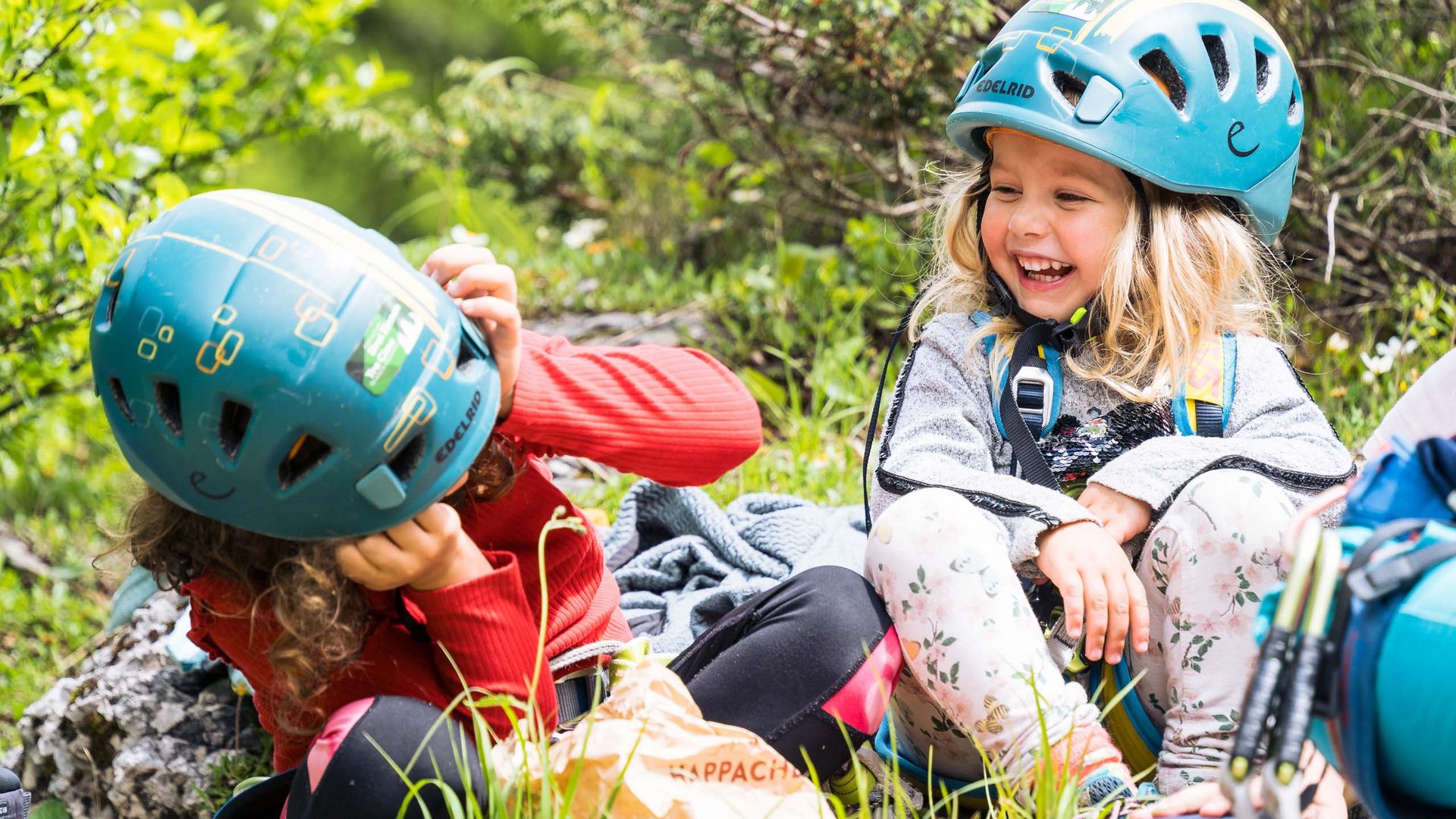 Qualche immagine del Rainer Due bambini con caschi da arrampicata ridono seduti sull'erba in natura