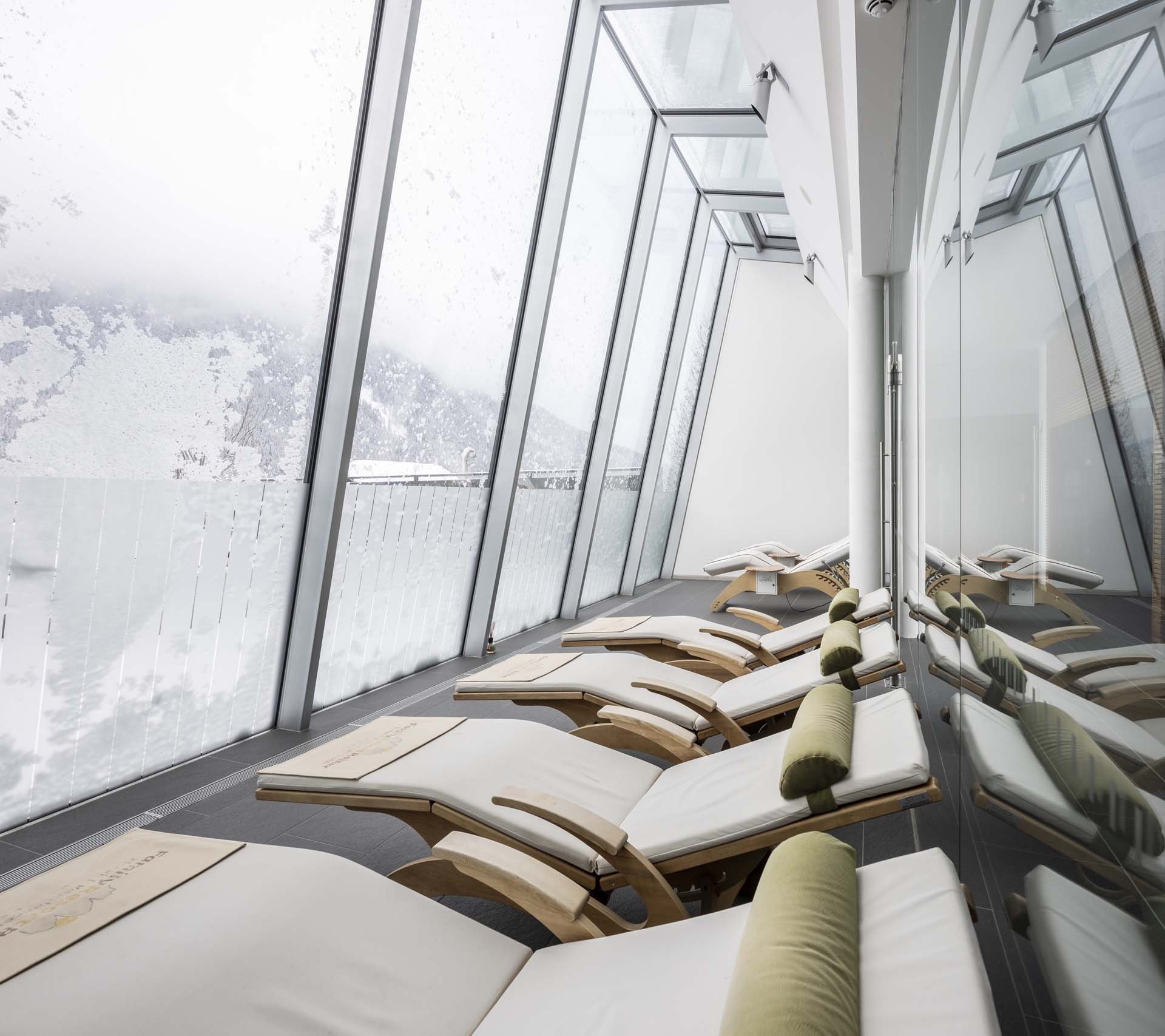 Property detail page - Hotel Rainer Lounge chairs in a modern spa room with large windows overlooking snowy mountains