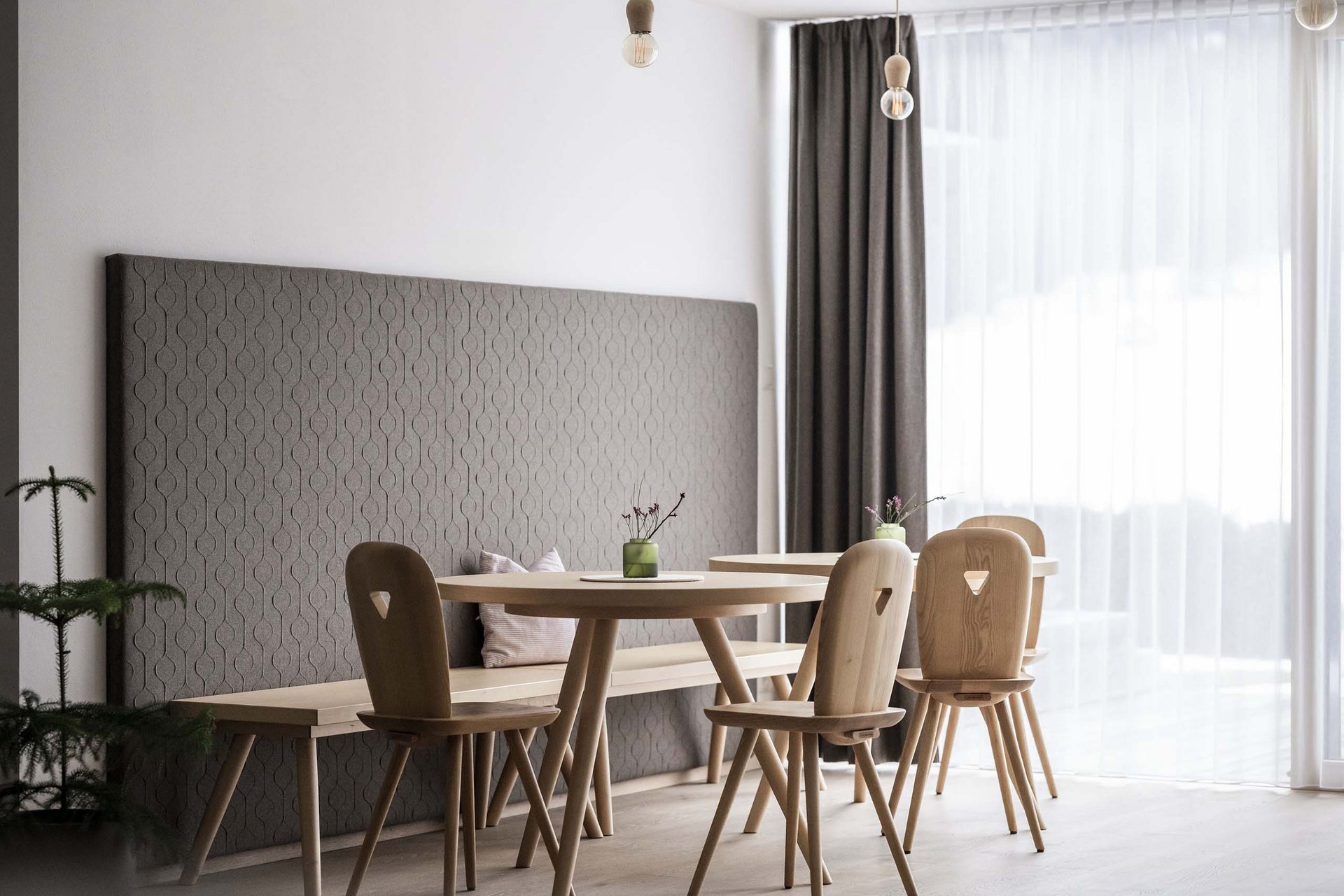 Naturerlebnis in der Villa Rainer Moderner Essbereich mit Holzstühlen und Rundtischen vor grauer Wand und großem Fenster