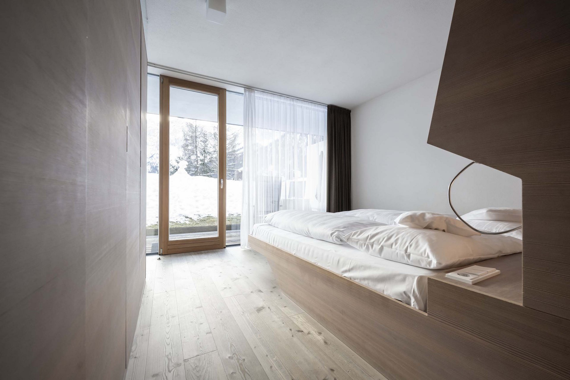 The Residence Königswarte Strata Minimalist bedroom with wooden bed and large window overlooking snow outside