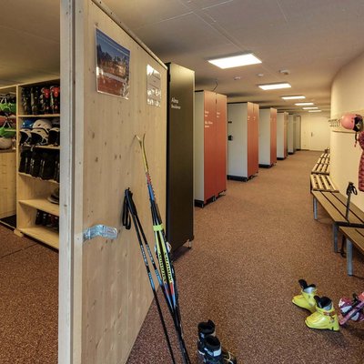 Deposito sci con caschi, scarponi e bastoncini in una stanza con armadietti