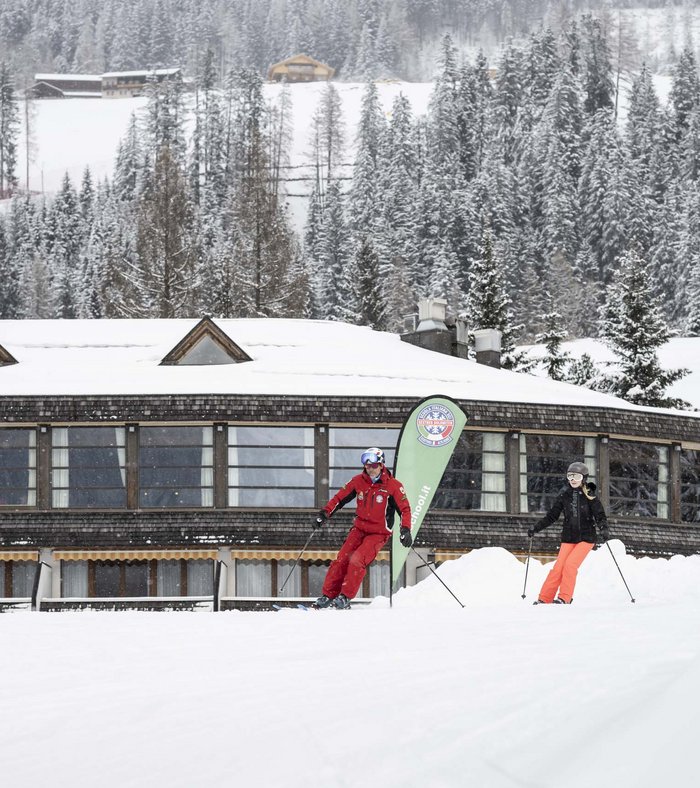Stay at the Rainer: Family holidays in the Dolomites! Ski instructor giving lesson in front of snowy building and forest