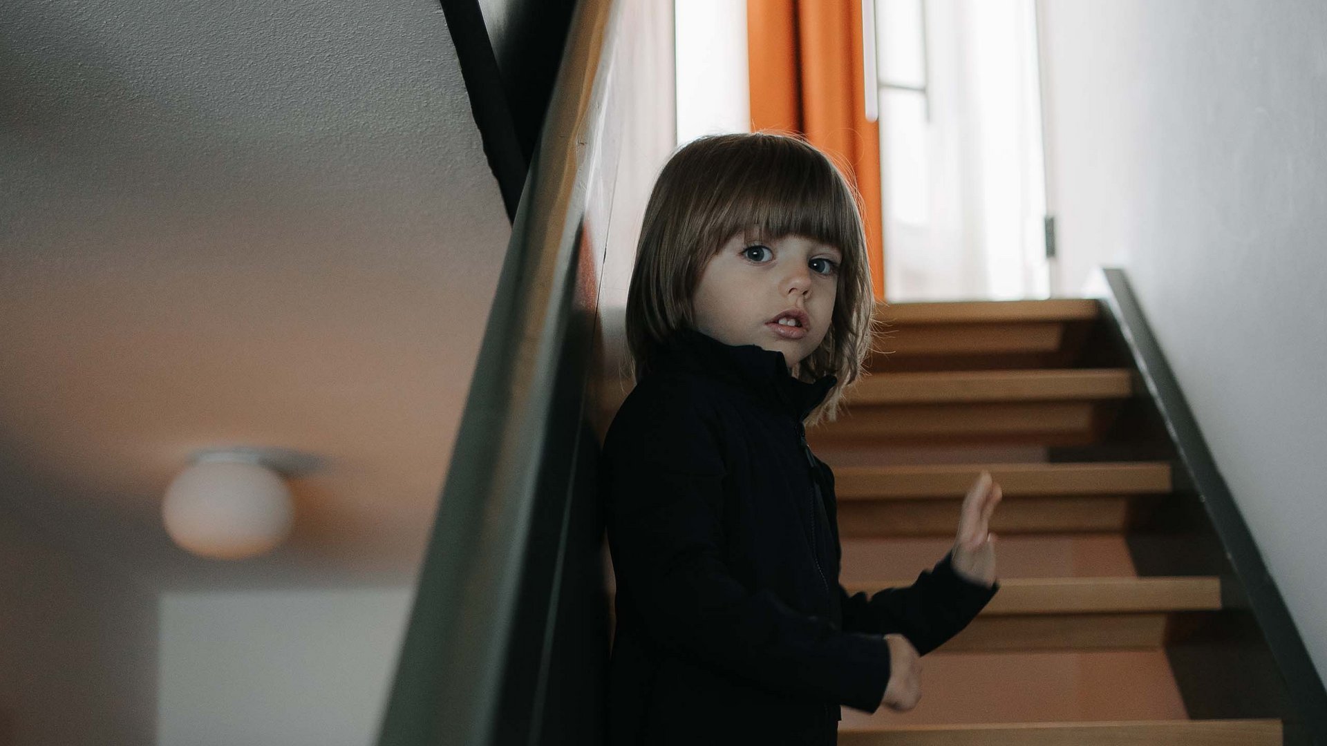 Family Resort Rainer Bambino in piedi su una scala di legno in casa che guarda verso la fotocamera