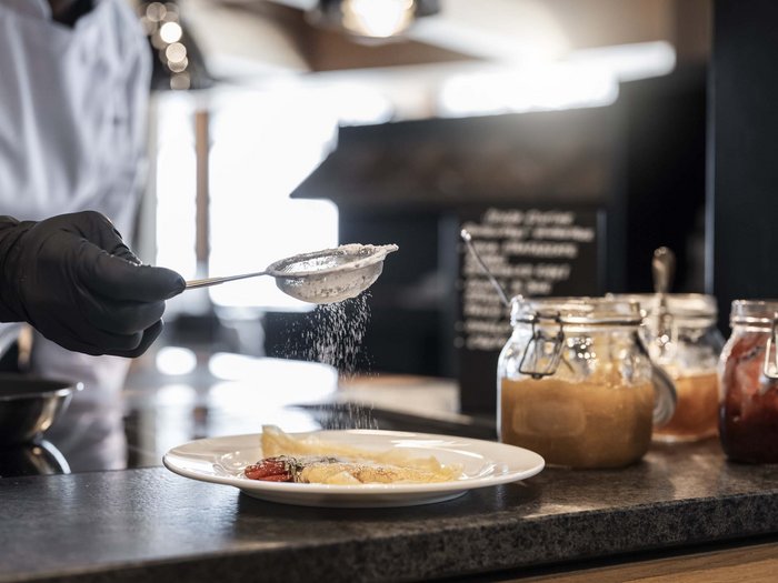 Gourmet delights from morning to night Hand with black glove sprinkling powdered sugar on pancake with jam