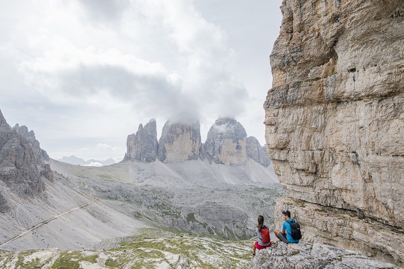 Suggerimenti esclusivi per i vostri tour Due escursionisti seduti su rocce con vista sulle Dolomiti e cielo nuvoloso