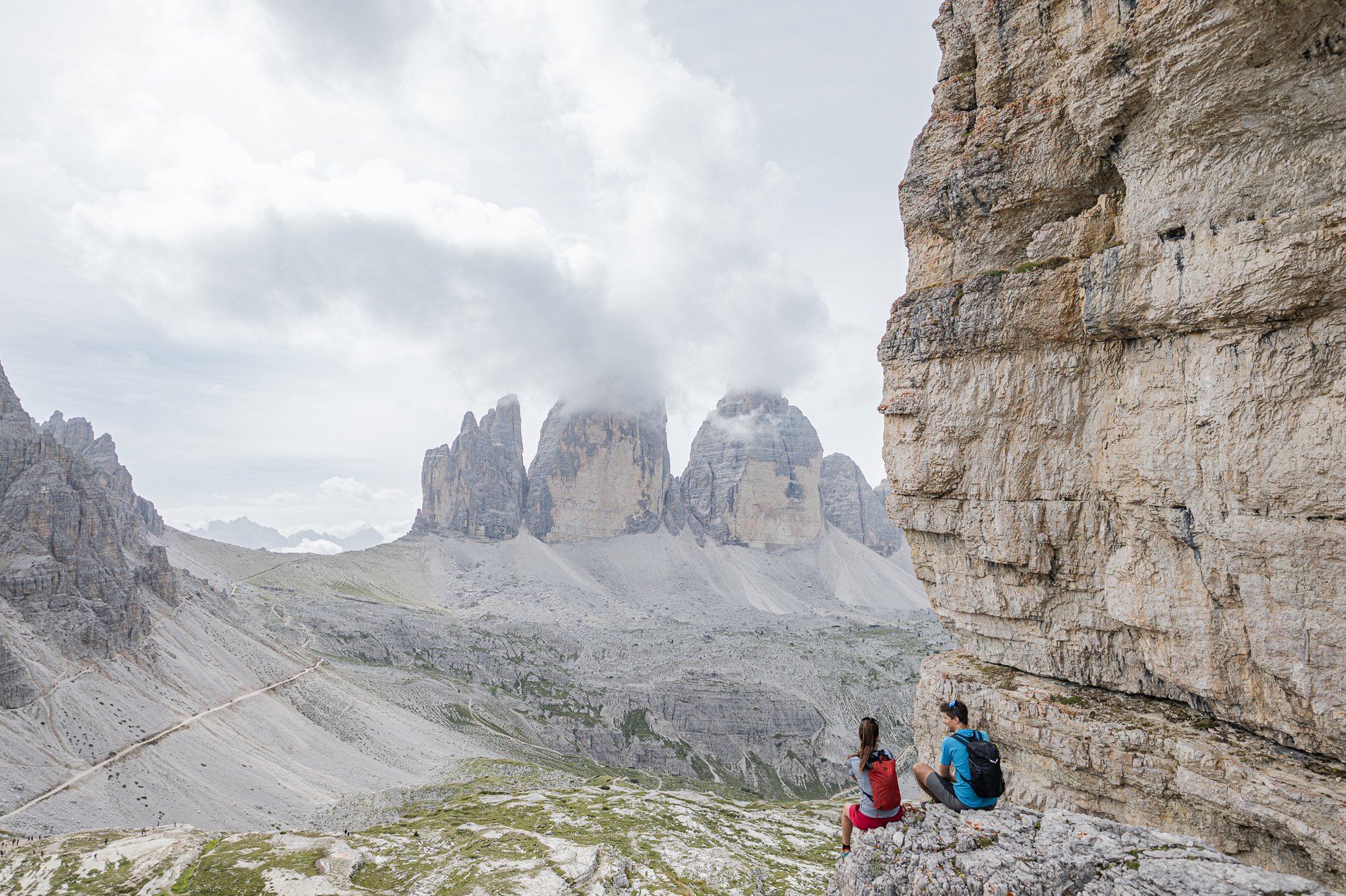 Escursione ai rifugi Due escursionisti seduti su rocce con vista sulle Dolomiti e cielo nuvoloso