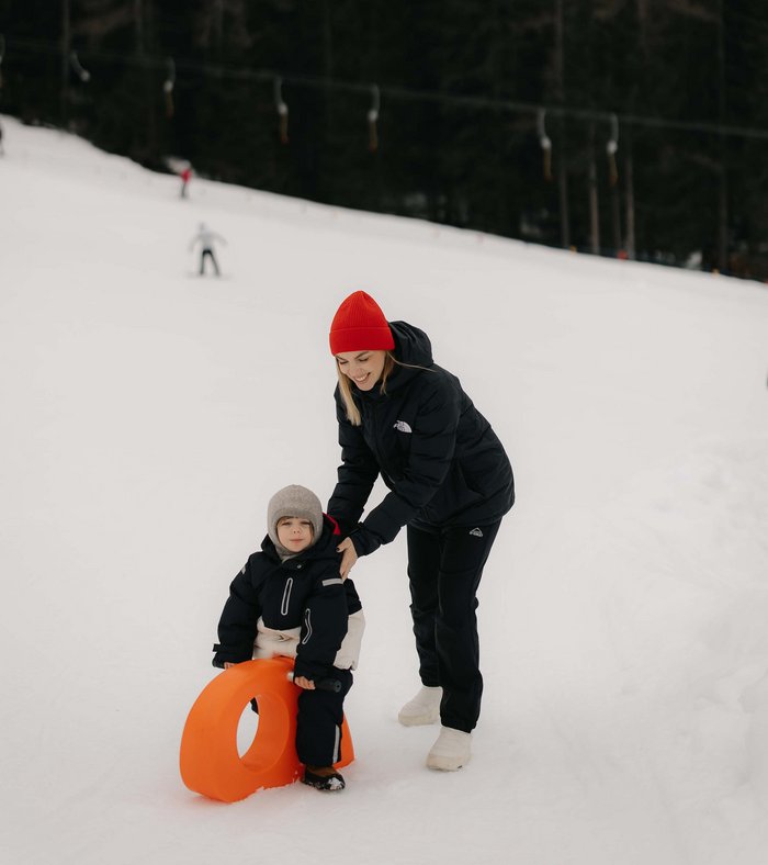 Family Resort Rainer: your accommodation in the Dolomites Woman helping child on orange sled in snowy landscape