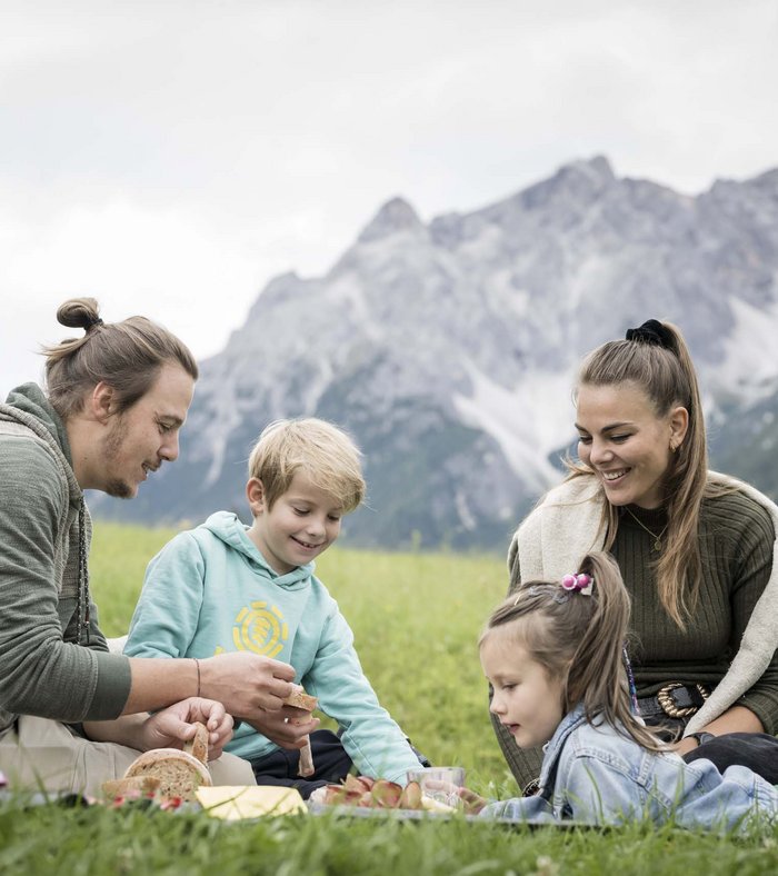 Il vostro family resort in Alto Adige Famiglia che fa un picnic su un prato con montagne sullo sfondo
