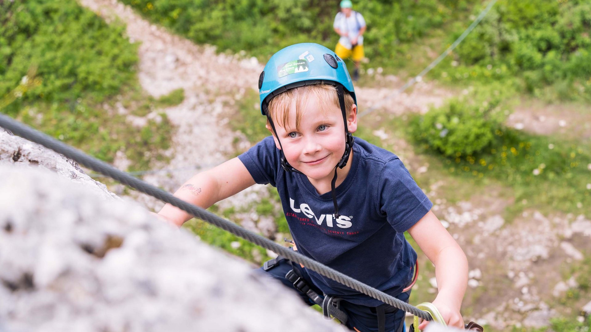 Qualche immagine del Rainer Bambino con casco arrampica una parete rocciosa, adulto assicura da sotto
