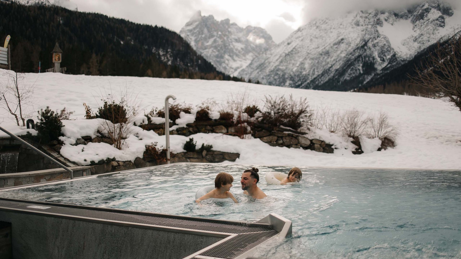 Family Resort Rainer Famiglia che nuota in piscina all'aperto con montagne innevate sullo sfondo