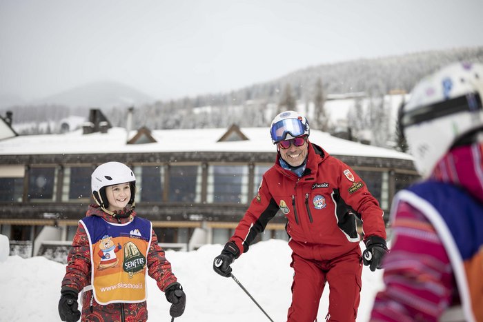 Stay at the Rainer: Family holidays in the Dolomites! Ski instructor teaching a smiling child in the snow in front of a mountain lodge