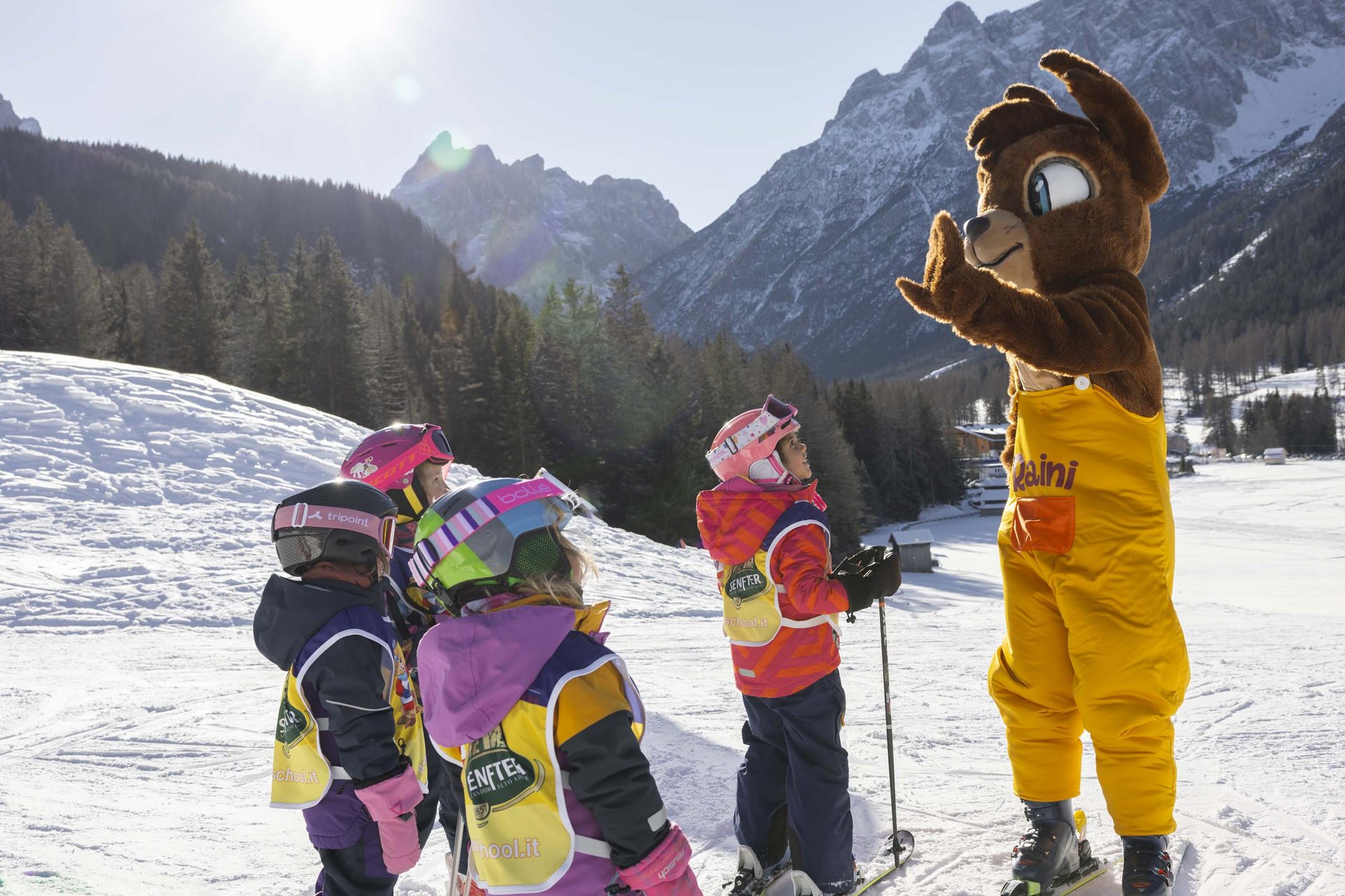 Ihr Familienresort in Südtirol Kinder in Skiausrüstung lernen mit einem Bärenmaskottchen im Schnee
