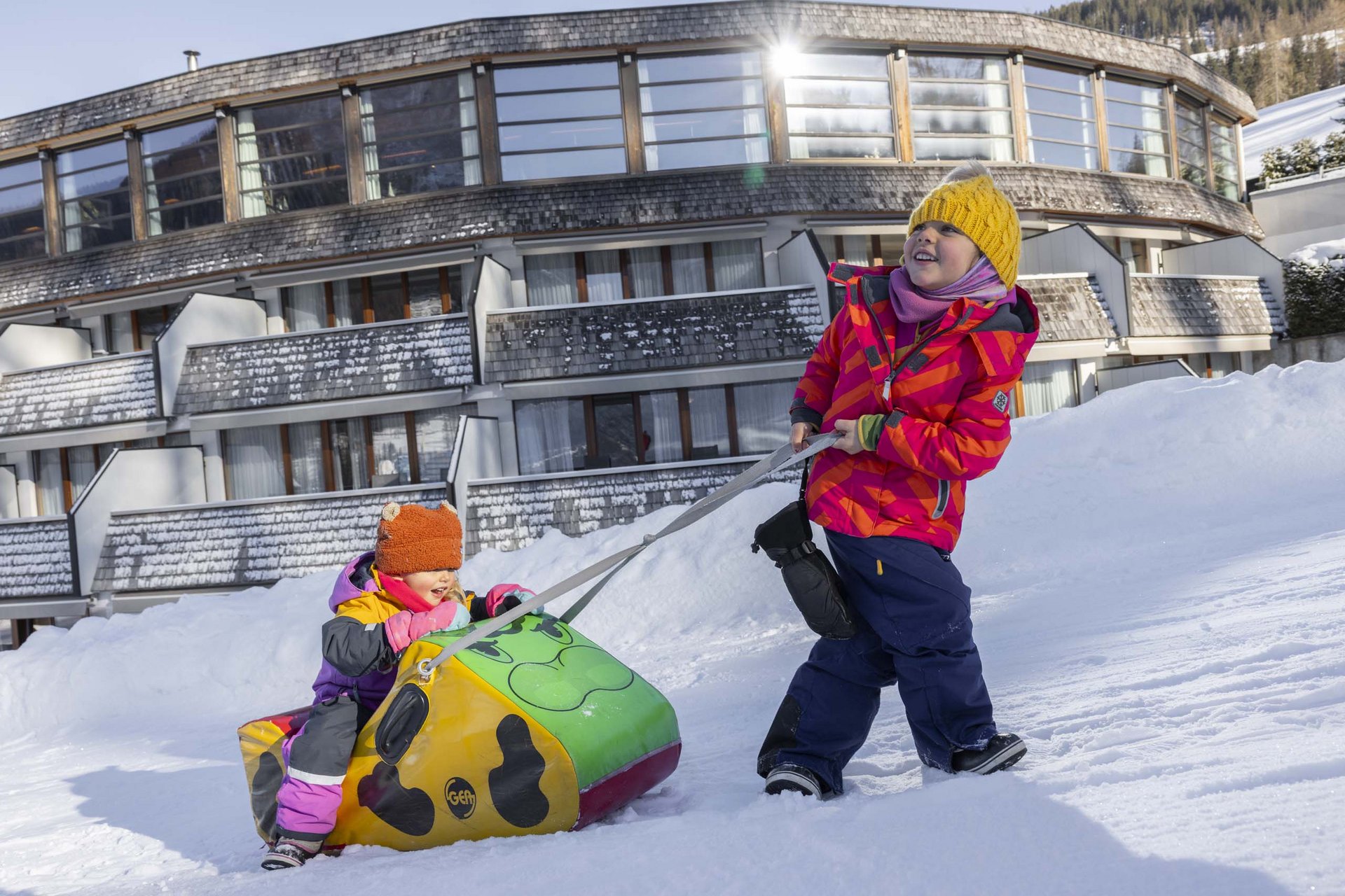 Ihr Familienresort in Südtirol Zwei Kinder spielen im Schnee vor einem großen Hotelgebäude