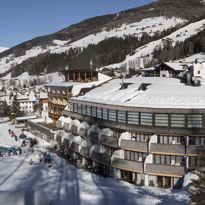 Ihr Familienresort in Südtirol Schnee bedecktes Hotel in verschneitem Bergdorf mit Menschen im Freien