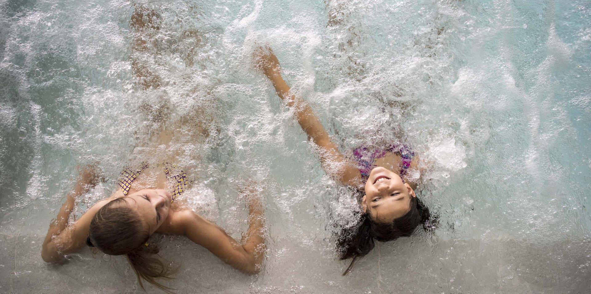 Zwei Mädchen entspannen lachend in einem Whirlpool mit Sprudelwasser