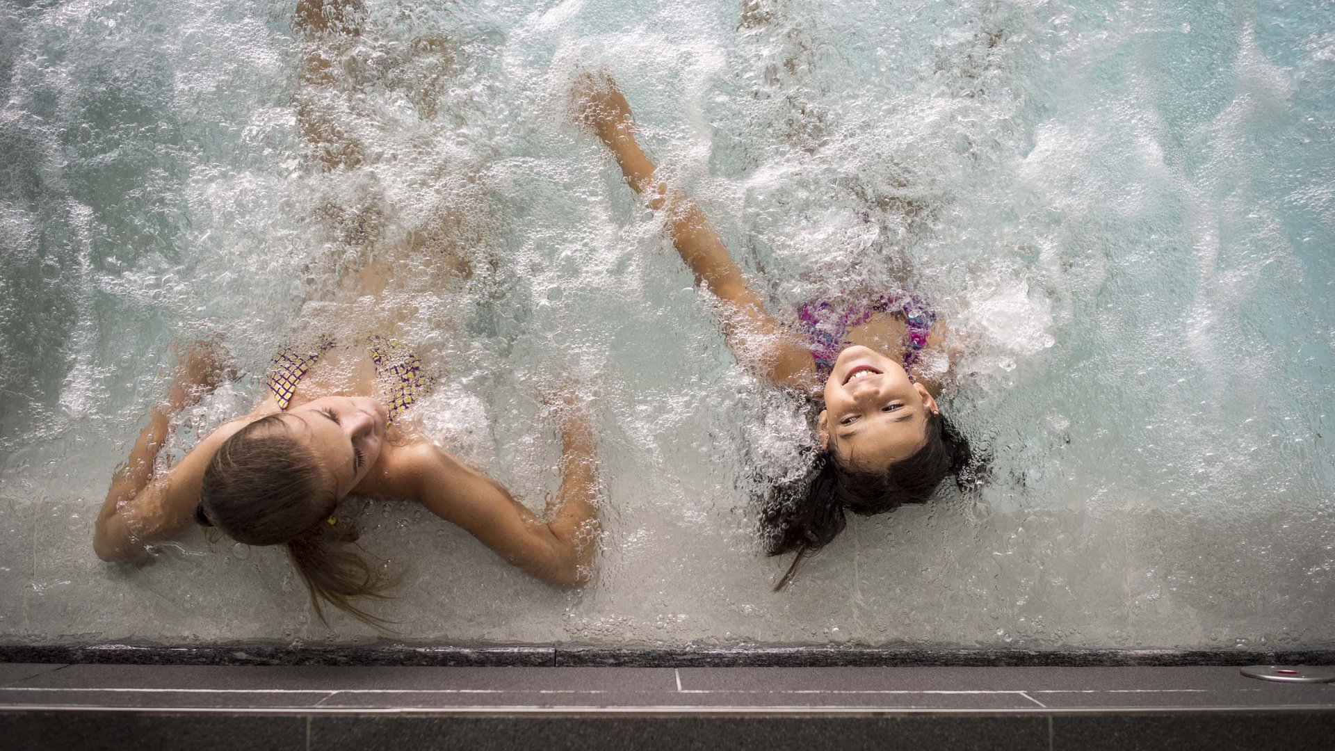 Family Resort Rainer Due bambine sorridenti rilassate in una piscina idromassaggio con acqua frizzante