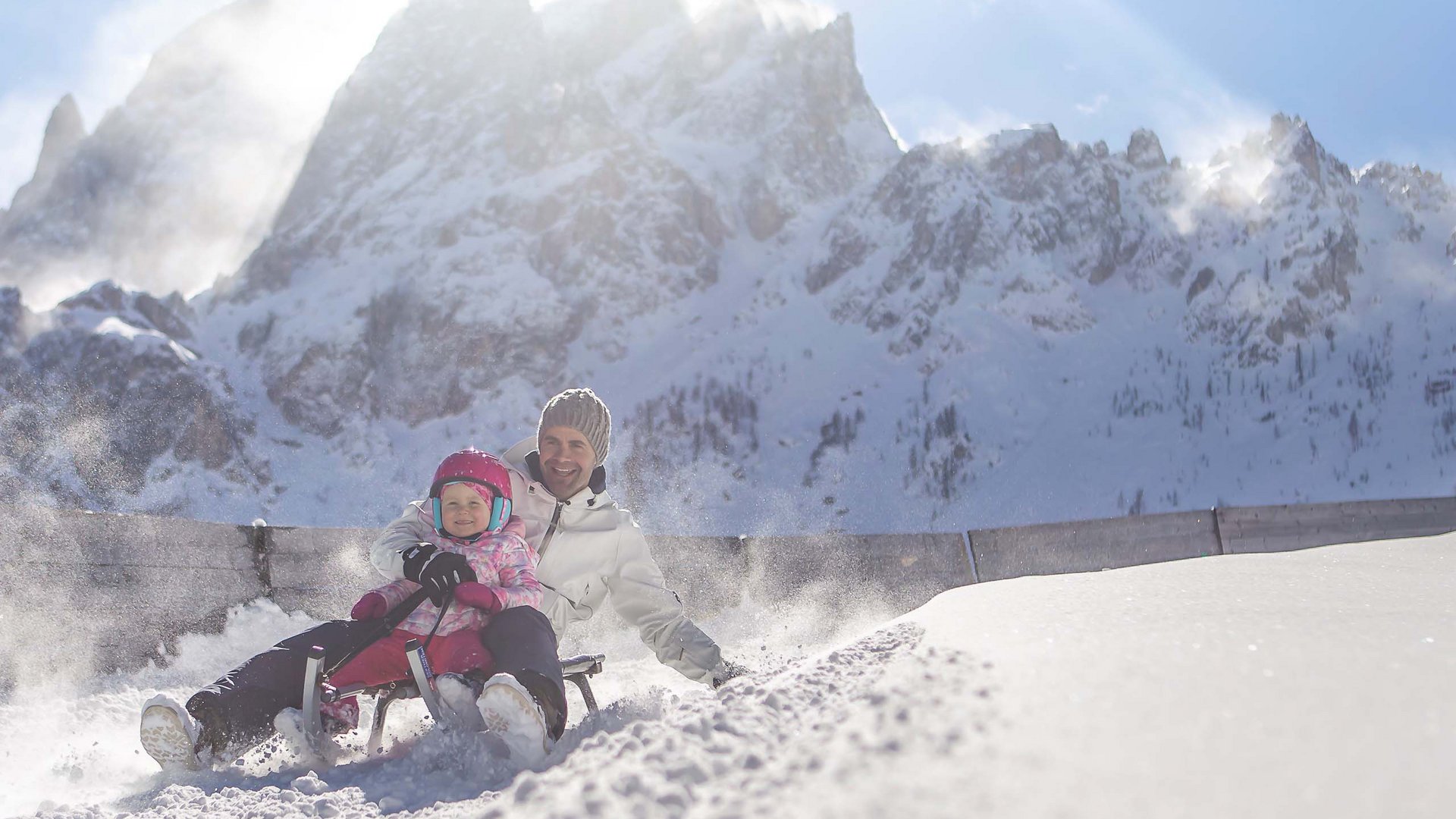 Qualche immagine del Rainer Padre e bambino slittano felici sulla neve davanti a montagne innevate