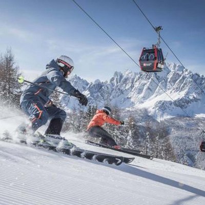 Ihr Familienresort in Südtirol Zwei Skifahrer auf verschneiter Piste mit Seilbahn und Bergkulisse