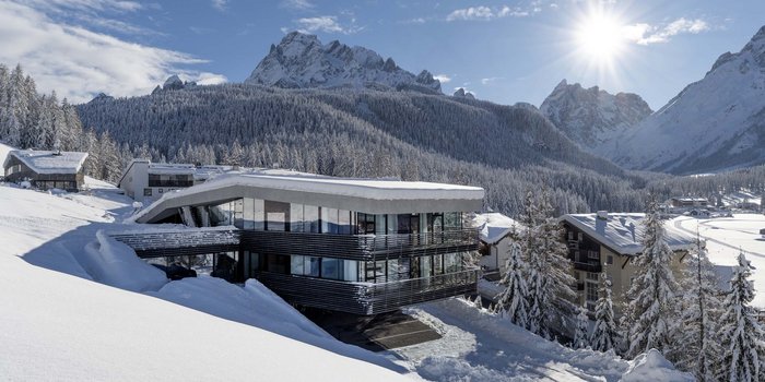 Rainer-Urlaub buchen in wenigen Klicks Modernes Hotel im Schnee vor verschneiten Bergen und klarem Himmel