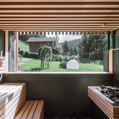 Relaxing wellness in the Dolomites: spa hotel in Sexten Modern sauna with wooden bench and large window overlooking green landscape