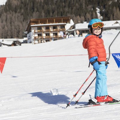 Puro divertimento al family hotel sulle piste da sci Bambino con casco e sci su neve davanti a un hotel di montagna