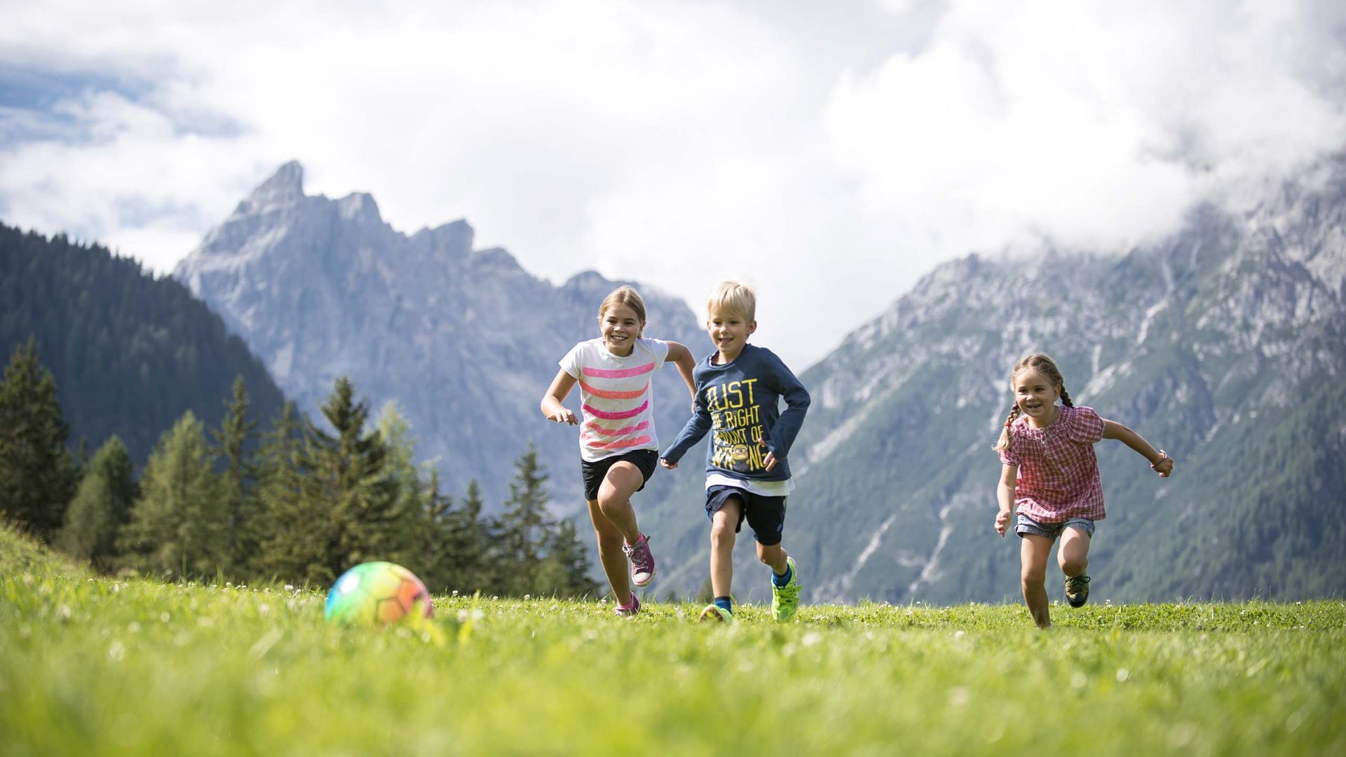 Qualche immagine del Rainer Tre bambini giocano a calcio su un prato con montagne sullo sfondo