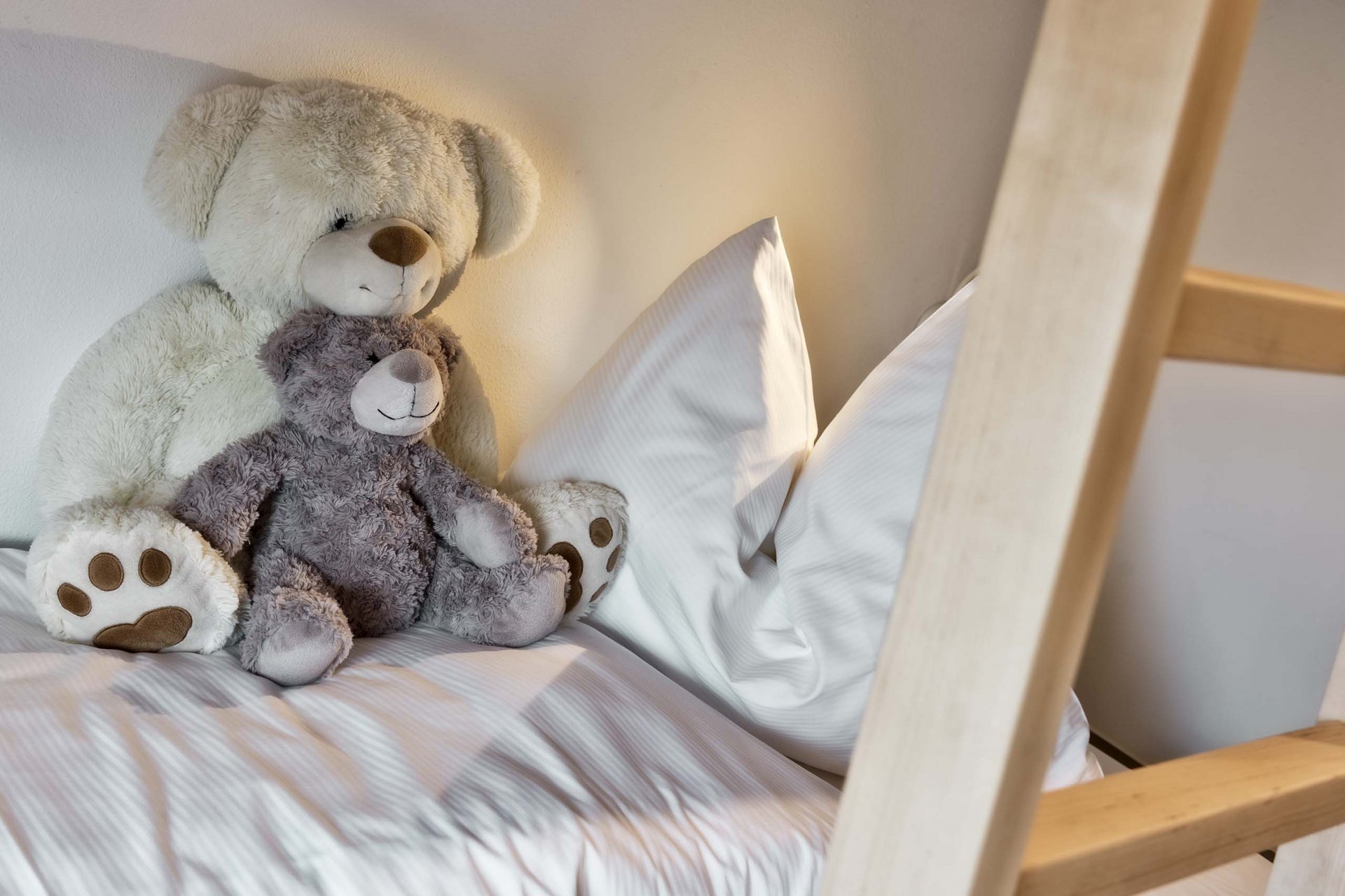 Naturerlebnis in der Villa Rainer Zwei Kuschelbären sitzen auf einem weißen Bett mit Kissen