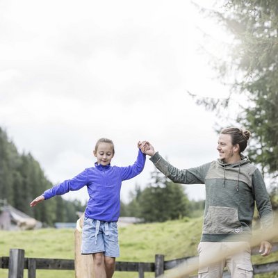 Ihr Familienresort in Südtirol Vater hilft Tochter beim Balancieren auf Slackline im Freien