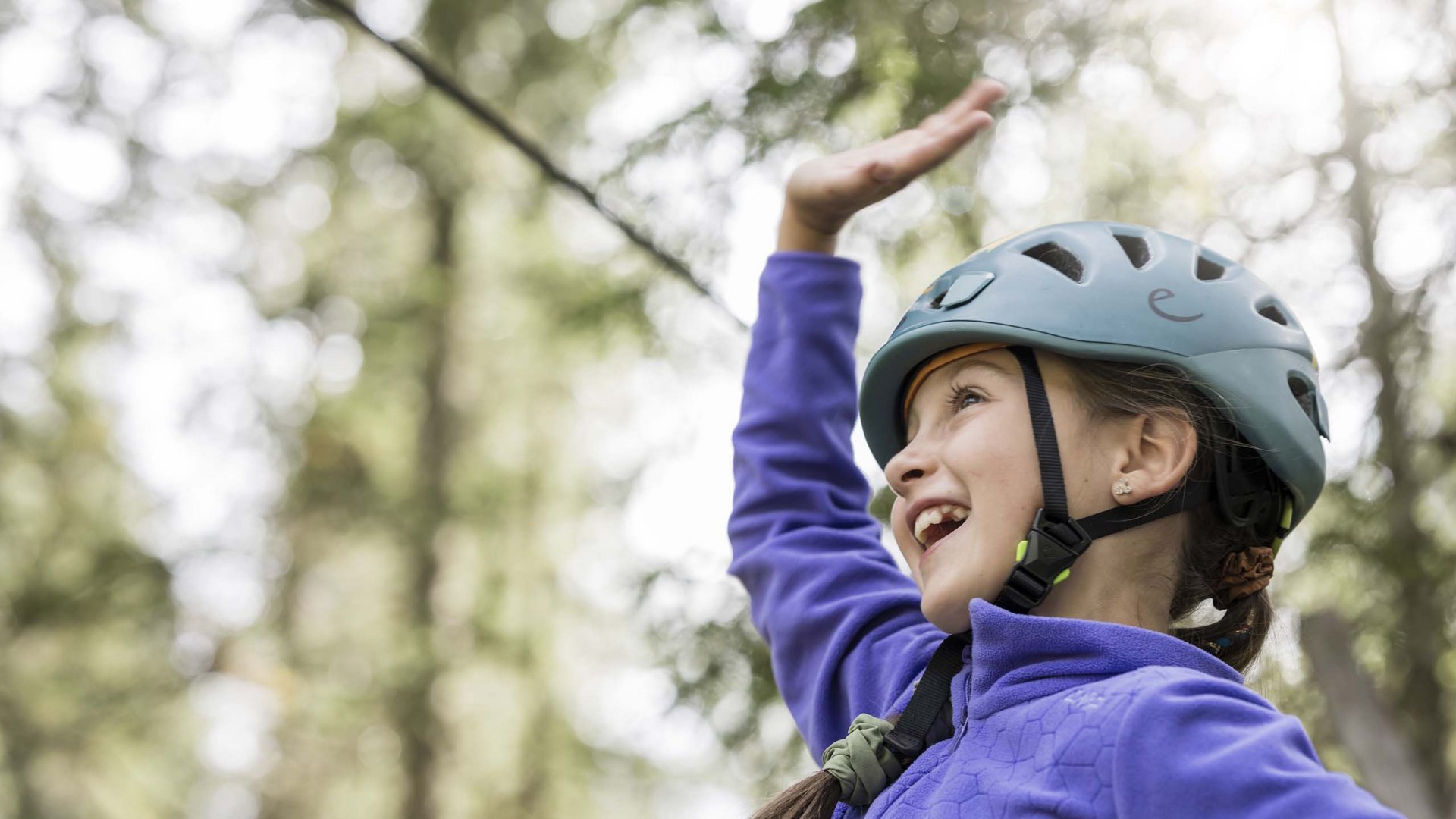 Your hotel with childcare in the Dolomites Girl wearing helmet raising hand while climbing in the forest