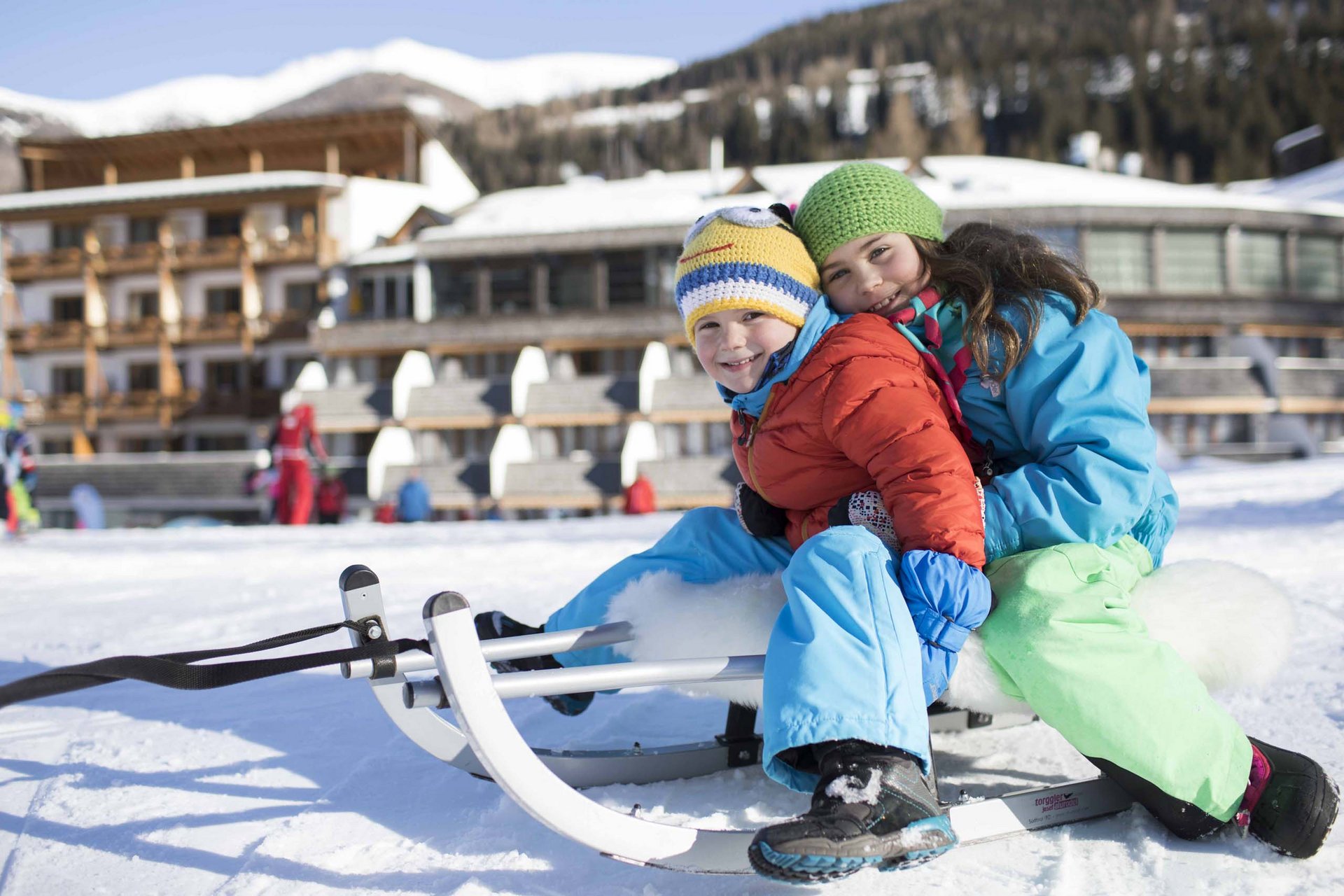 Due bambini sulla slitta sulla neve davanti a un hotel