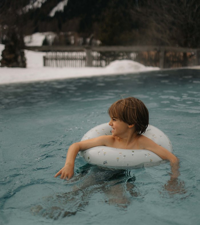 Your fulfilling family holiday Boy swimming with float ring in outdoor pool with snowy landscape around