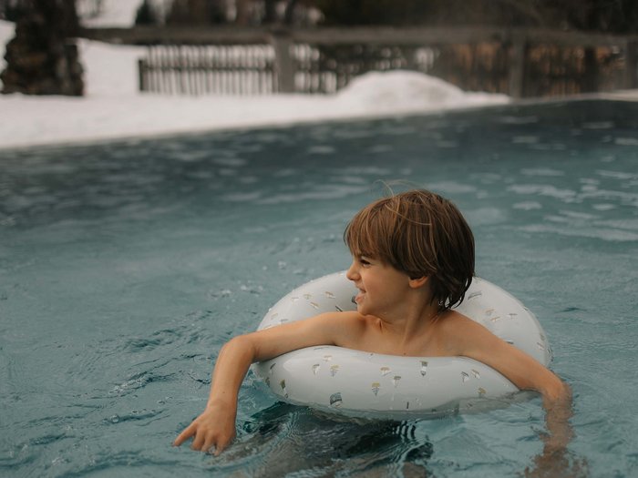Your hotel with childcare in the Dolomites Boy swimming with float ring in outdoor pool with snowy landscape around