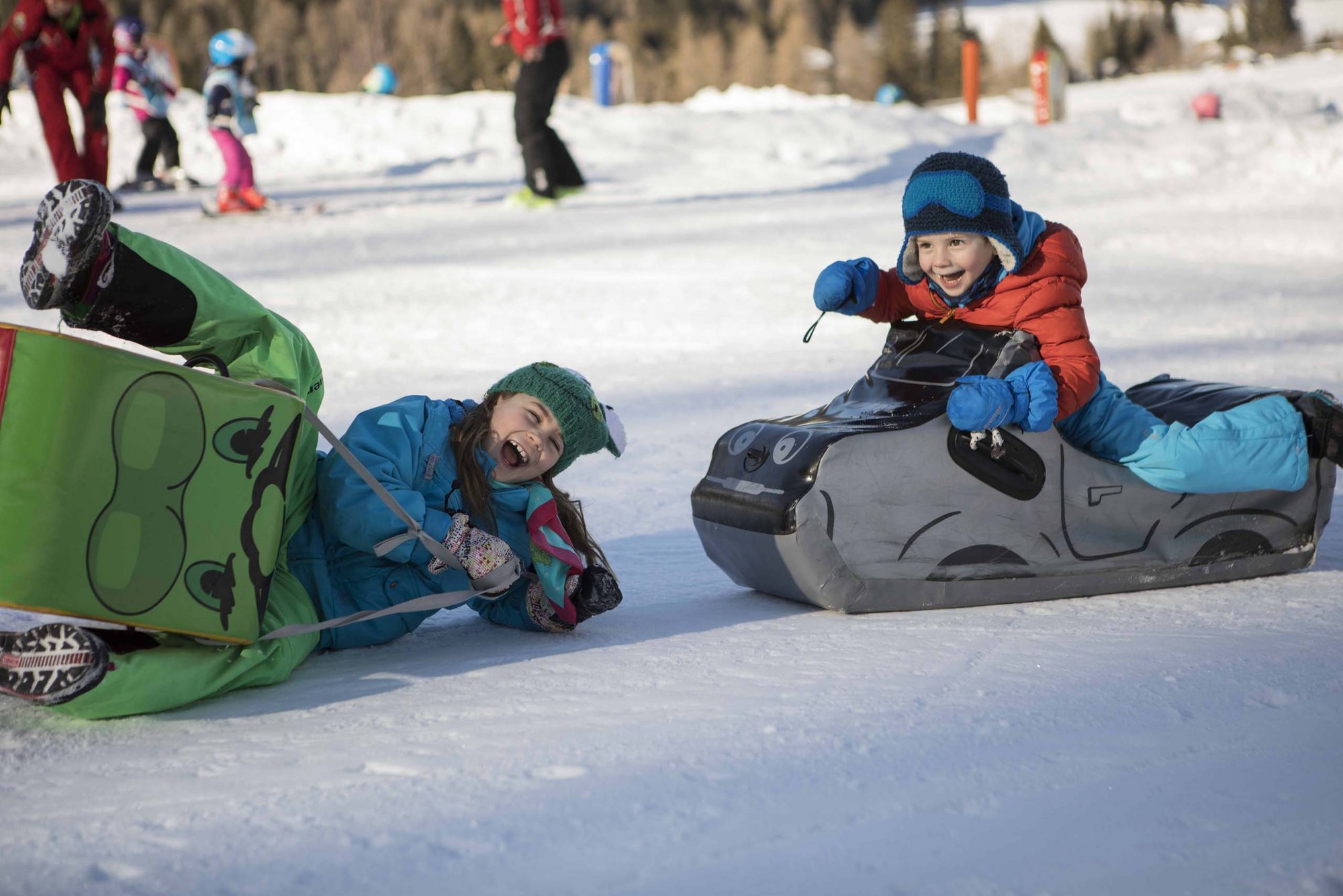 Stay at the Rainer: Family holidays in the Dolomites! Children laughing and playing with inflatable sleds on the snow