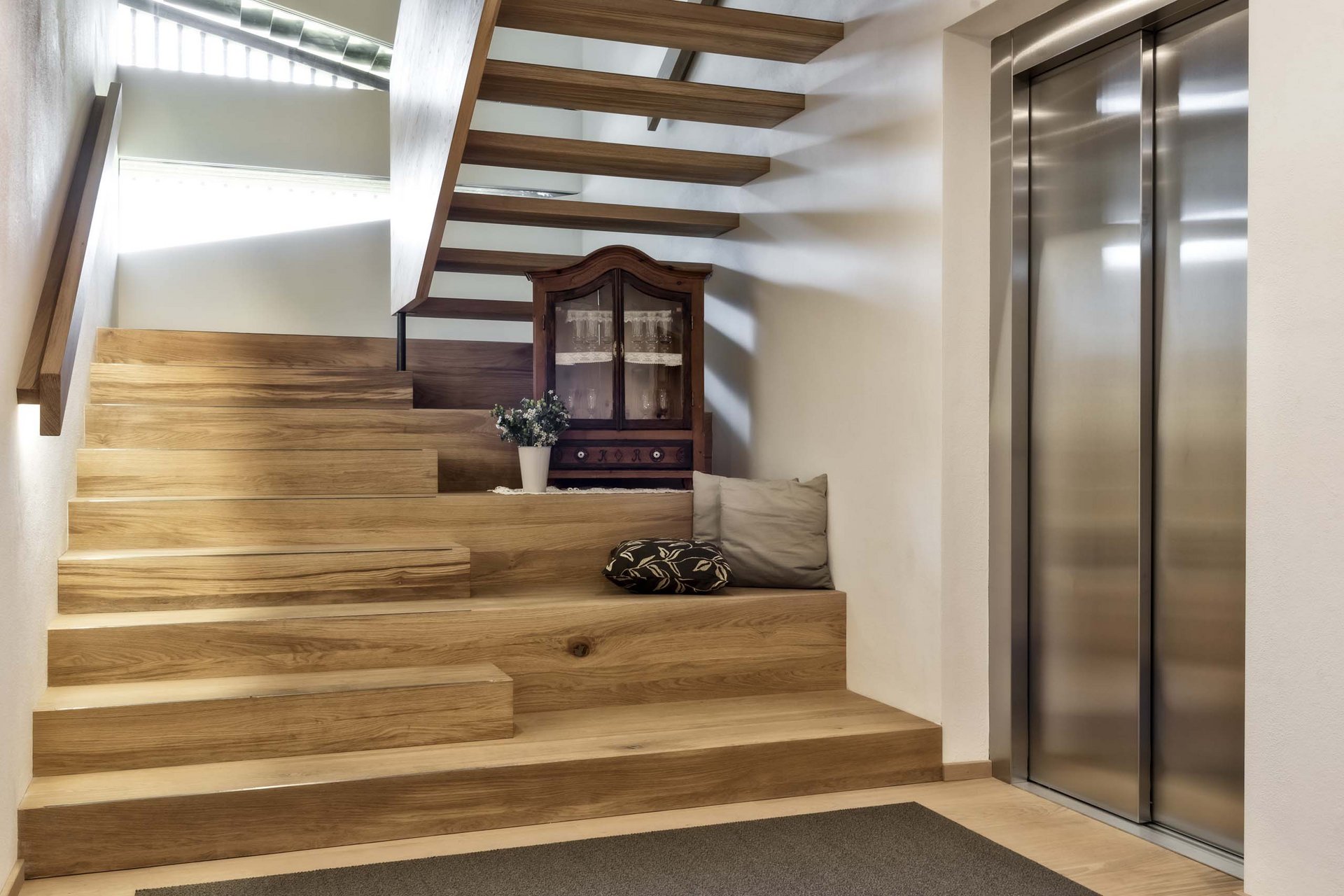 Naturerlebnis in der Villa Rainer Moderner Innenraum mit Holztreppe, Sofakissen, Vitrine und Aufzug mit Edelstahltür
