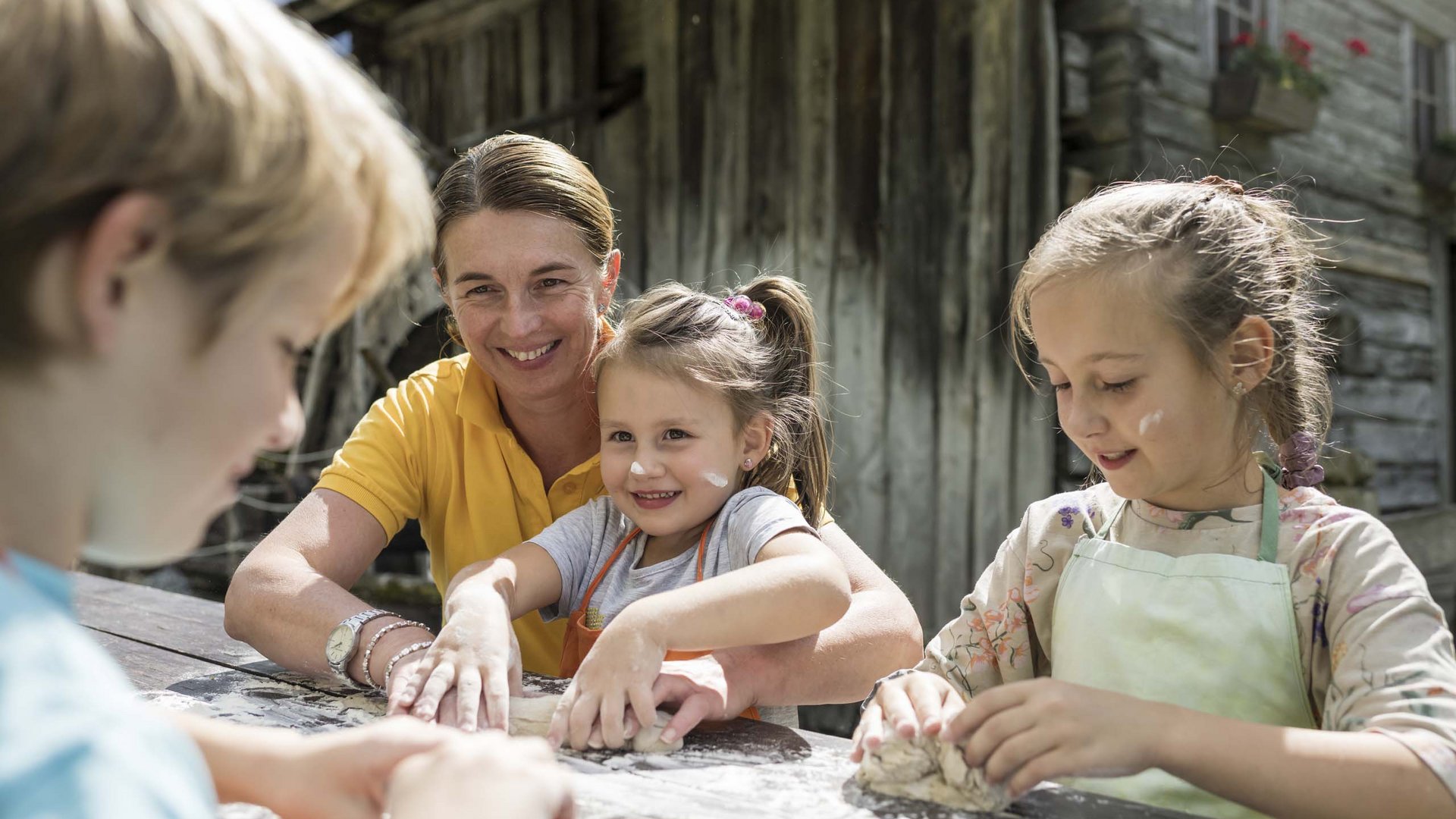 Qualche immagine del Rainer Donna aiuta bambini a impastare la pasta su un tavolo di legno all'aperto