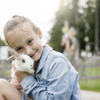 Ihr Familienresort in Südtirol Mädchen umarmt Kaninchen im Freien in einem Park