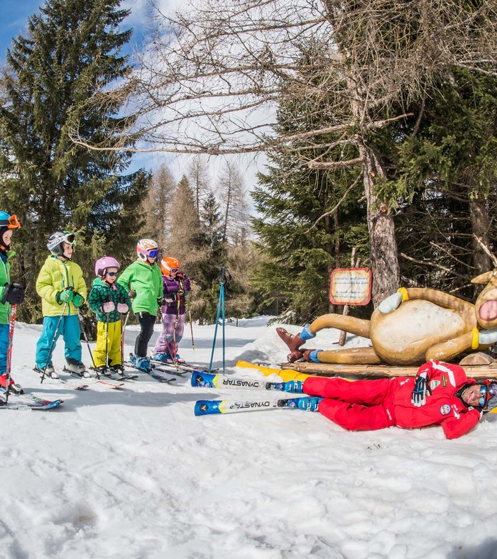 Children skiing with instructor next to a funny reindeer figure in the snow