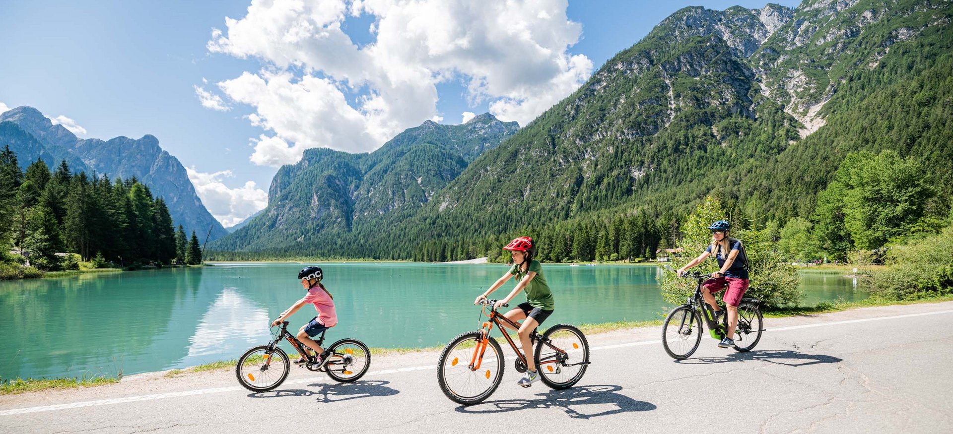 La località perfetta per la mtb: Sesto Tre persone in bicicletta vicino a un lago circondato da montagne in una giornata soleggiata