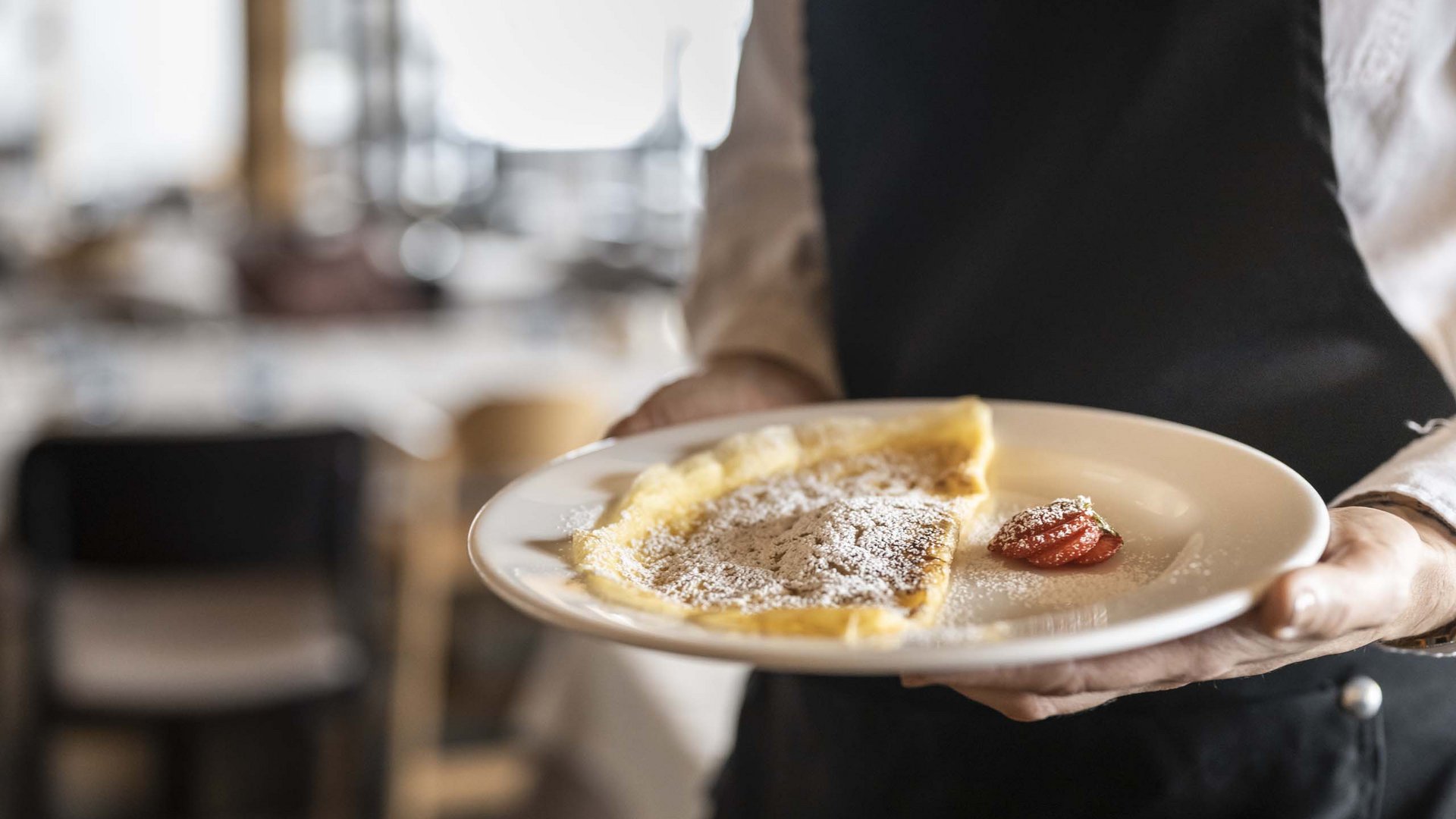 Family Resort Rainer Cameriere serve crepe con zucchero a velo e fragola su un piatto