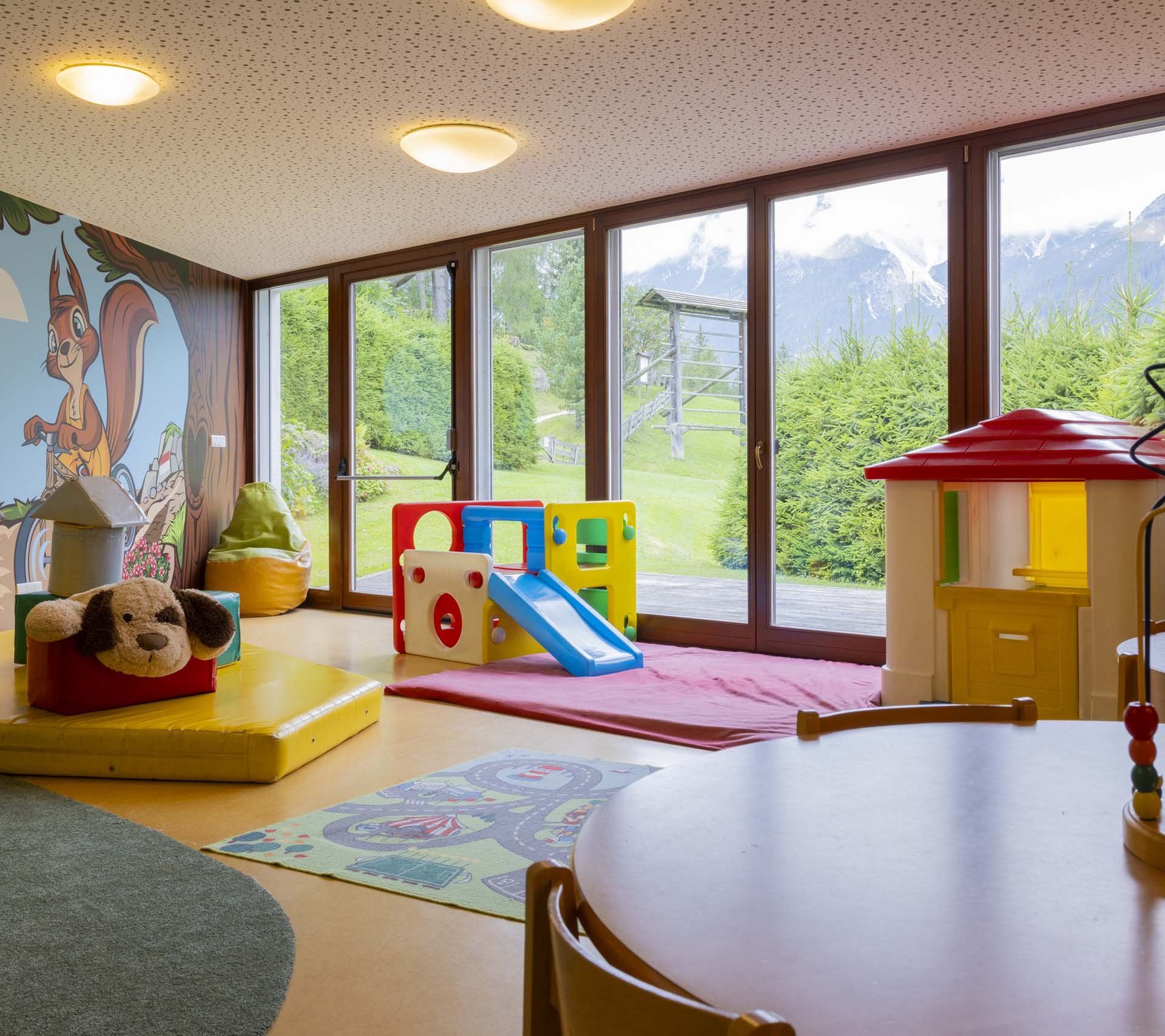 Property detail page - Hotel Rainer Children's playroom with playhouse, slide, and large windows showing mountain view