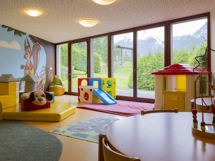 Sala giochi per bambini con casetta, scivolo e ampie finestre con vista sulle montagne