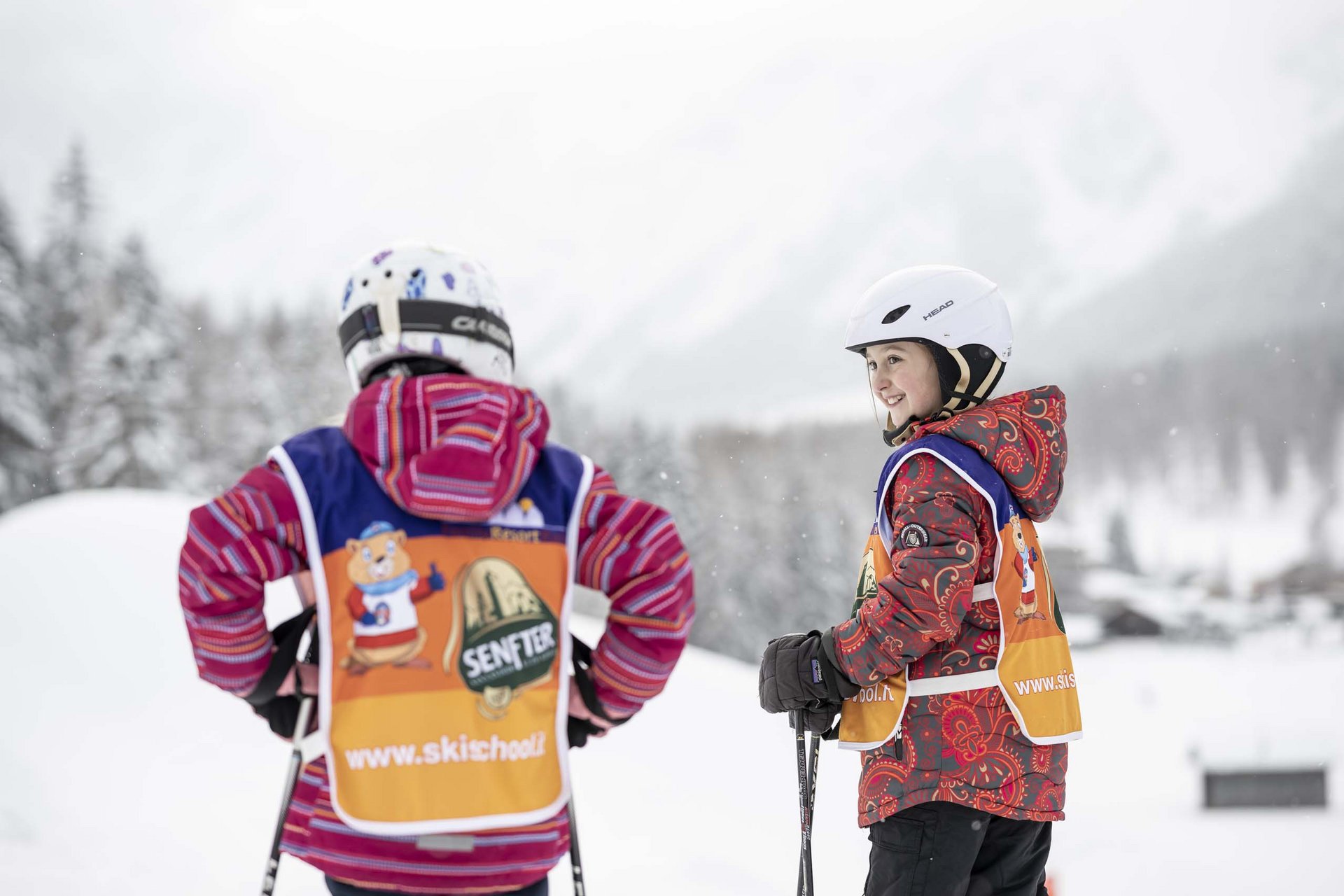 Due bambini alla lezione di sci con caschi e bastoncini sulla neve